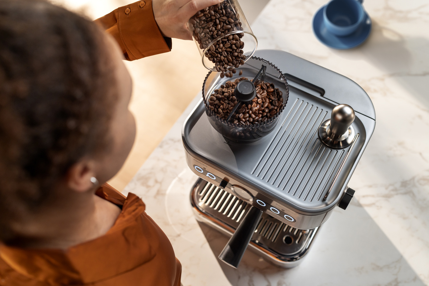 Mlad&aacute; d&aacute;ma sype zrnkov&uacute; k&aacute;vu do z&aacute;sobn&iacute;ka na zrnkov&uacute; k&aacute;vu k&aacute;vovaru Philips Barista Brew